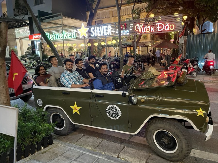 Team members riding a vintage jeep through Hanoi at night